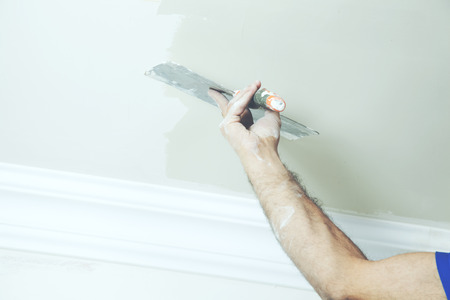 Closeup of repairman hand plastering a wall with putty knife or spatulaの写真素材