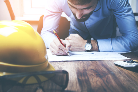 cropped image of a young male architect working on blueprints spread out on a tableの写真素材