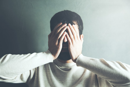 Depressed man hand in face on dark background