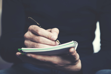 A man is sitting on a sofa and writing notes in a notebookの写真素材