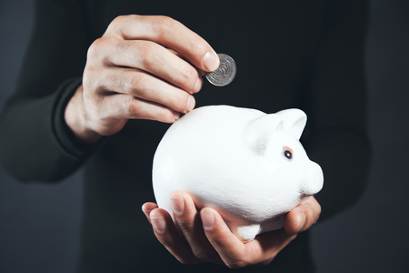 Business man putting coin into the piggy bankの写真素材