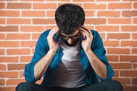 sad man hand in head on brick wall backgroundの写真素材