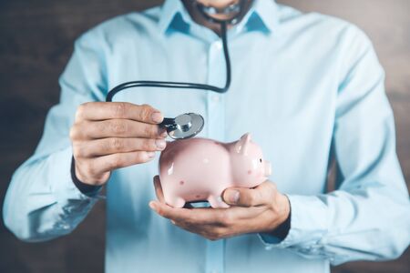 man hand holding  stethoscope and piggy bank