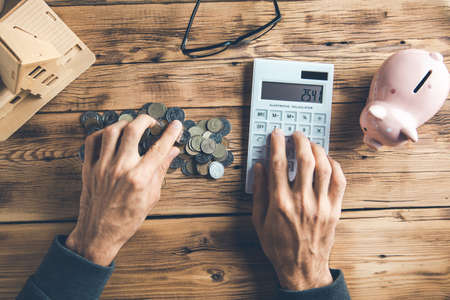 man hand coins with calculator and house model on desk