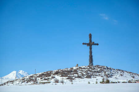 cross on icy mountain in the winter season under skyの写真素材