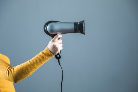 woman hand holding hair dryer on gray backgroundの写真素材