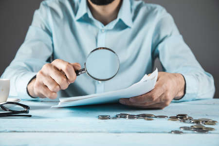 man hand magnifier and document with coins on the table