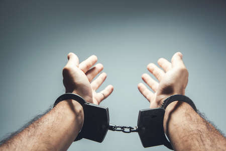 Close up of handcuffed hands on a gray backgroundの写真素材