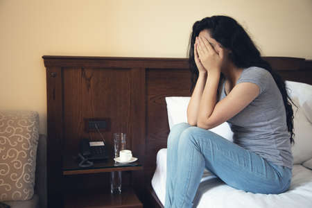 sad woman sitting on the bed in the hotelの写真素材