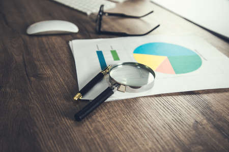 magnifier with glasses on graph and keyboard on deskの写真素材