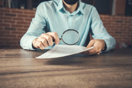 Businessman readng documents with magnifying glass in officeの写真素材