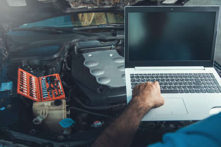 Professional car mechanic working in auto repair service using laptop on carの写真素材