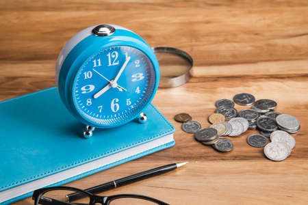 clock on book with coins on the tableの写真素材