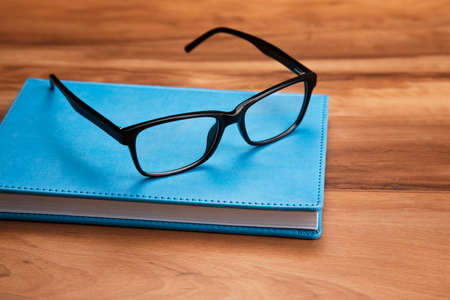 black glasses on blue book in wooden table.の写真素材