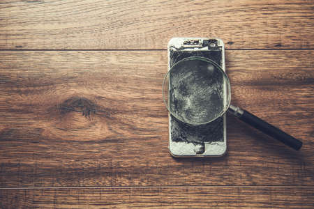 broken phone and magnifier on the tableの写真素材