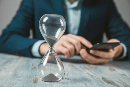 man holding phone with hourglass on table