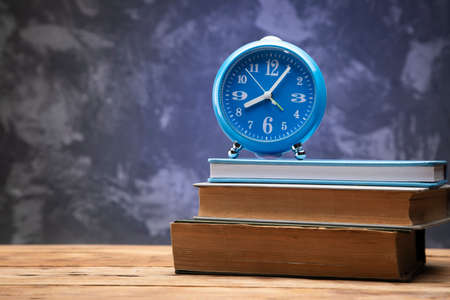 blue clock on the books on wooden table