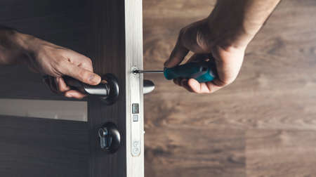 The man is installing the part of the wooden door by the screwdriver