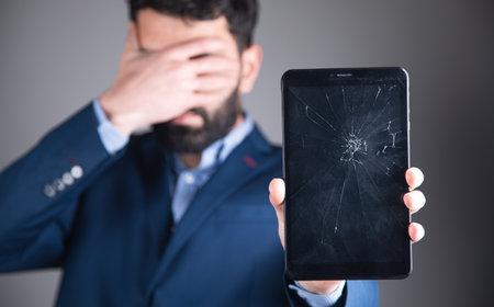 young sad man holding broken screen tabletの写真素材
