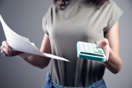 Business woman counting on calculator and holding documents in handsの写真素材