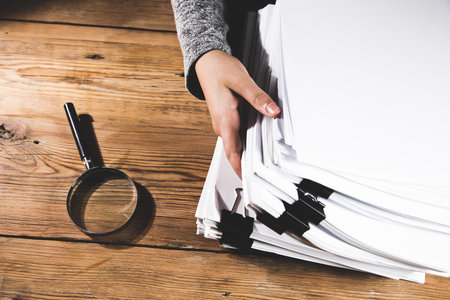 woman holding stack of files with magnifier on the table