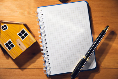Blank notebook and house model on brown wooden background. Real estate conceptの写真素材
