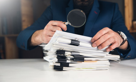 Businessman looking through a magnifying glass to documents