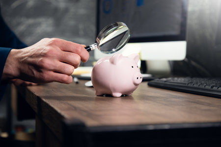 man examines a piggy bank with a magnifying glassの写真素材
