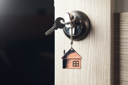 House key on a house shaped silver keyring in the lock of a doorの写真素材