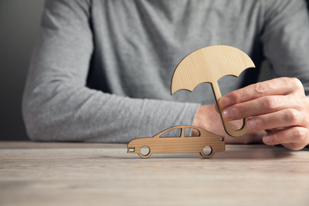 Businessman hand holding umbrella and cover car toy on table. Car insuranceの写真素材