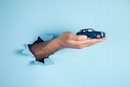 hand of man hold miniature toy car on the blue background. automobile and transportation conceptの写真素材
