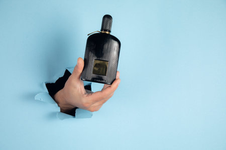 bottle of perfume in a man hand on blue background