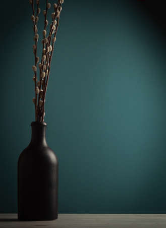 Still life with black vase and willow on a blue-green background with a gradient, copy space, vertical orientation, vignetteの写真素材