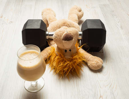 Fitness concept - sports and fitness at home - tired stuffed toy under hexagon dumbbell and coffee, horizontal orientationの写真素材