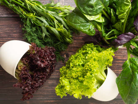 different edible fresh herbs, greens of green and purple in white pots and on a wooden table, top...