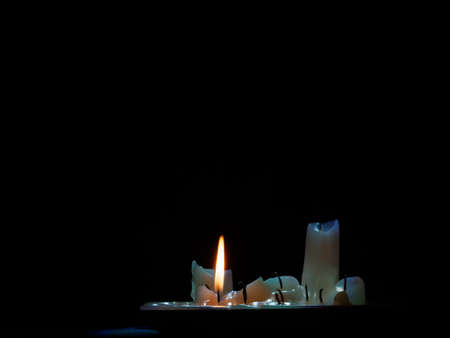 a group of burned out candles, one still burning in the darkの写真素材