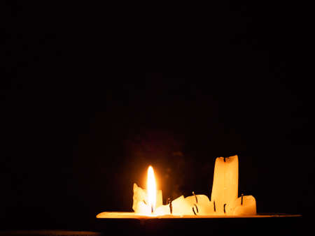 a group of burned out candles, one still burning in the darkの写真素材
