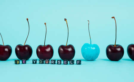 Inscription "be yourself", composed of small letters-beads background of berries of cherries standing in formation, one of which is painted in blue. Focus on letters. Freedom conceptの写真素材