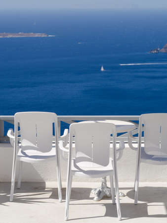 three white chairs with white table on the white terrace with blue sea view on a sunny day, without peopleの写真素材