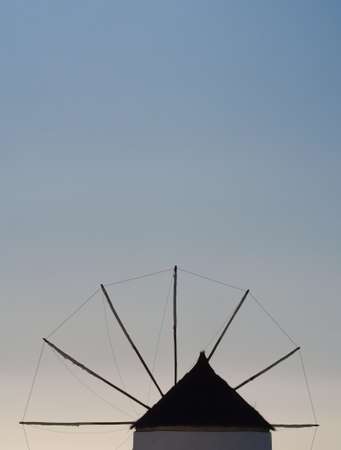 silhouette of a greek windmill with a triangular roof against a pale blue sky, vertical orientation