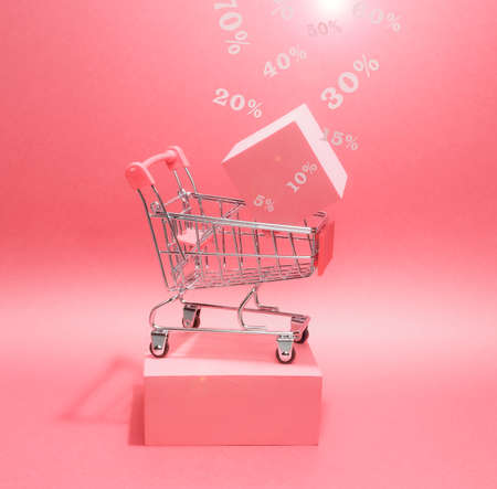 Photo of a bright podium (pedestal) of shopping cart on a paper background. In the cart cube and levitating percent signs. In pink, with gradient and glare.の写真素材