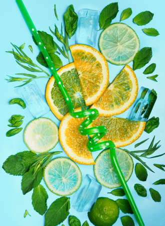 Sliced circles of lemon and orange with leaves of mint and basil on a blue background. Lemonade concept with ice.の写真素材