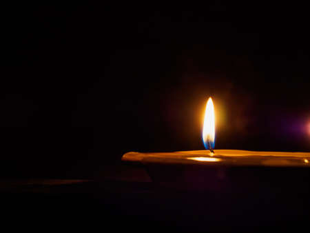 the flame of a lonely burning candle in a puddle of wax in the darkの写真素材