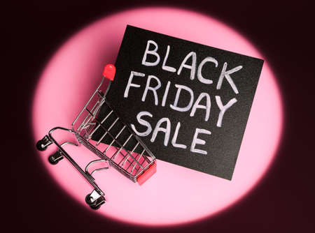 flat lay of black chalk board with chalk lettering "black friday sale" in a shopping cart on a pink background with dark circular vignetteの写真素材