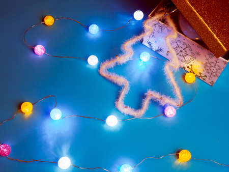 gift gold box, white christmas tree and lighted garland on blue backgroundの写真素材