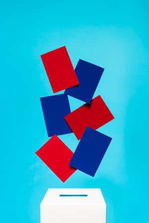 election concept - blue and red cards fall into a white voting box with a slot, the background is blue, levitationの写真素材