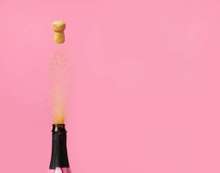 holiday concept - the salute from the bottle - a cork and golden confetti are shoots of a bottle of champagne, on a pink backgroundの写真素材