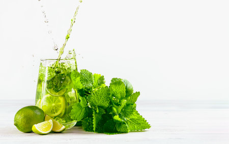 Mojito pours into a glass with splash on a light background, two jets, with limes, a bunch of mint and ice. One of set mojito.の写真素材