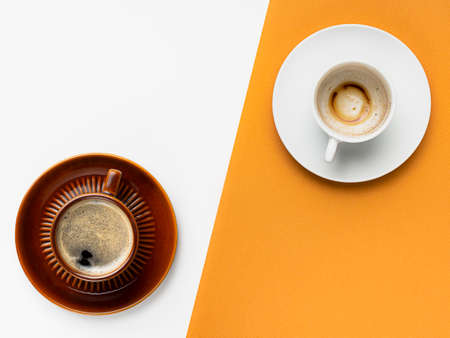 Two cups of coffee, one brown cup of black coffee on white background, the other is empty used coffee cup on orange background, contrast, breakfast concept. Cup and saucer.の写真素材