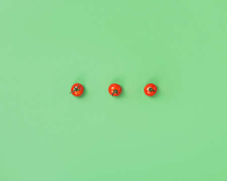 three red cherry tomatoes on a green background, top view, minimalism